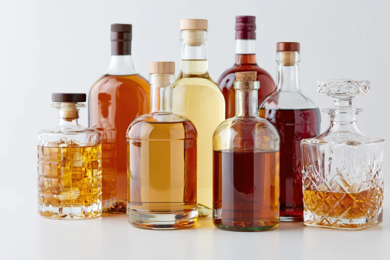 Assorted liquor bottles and a crystal decanter arranged in a row on a white surface
