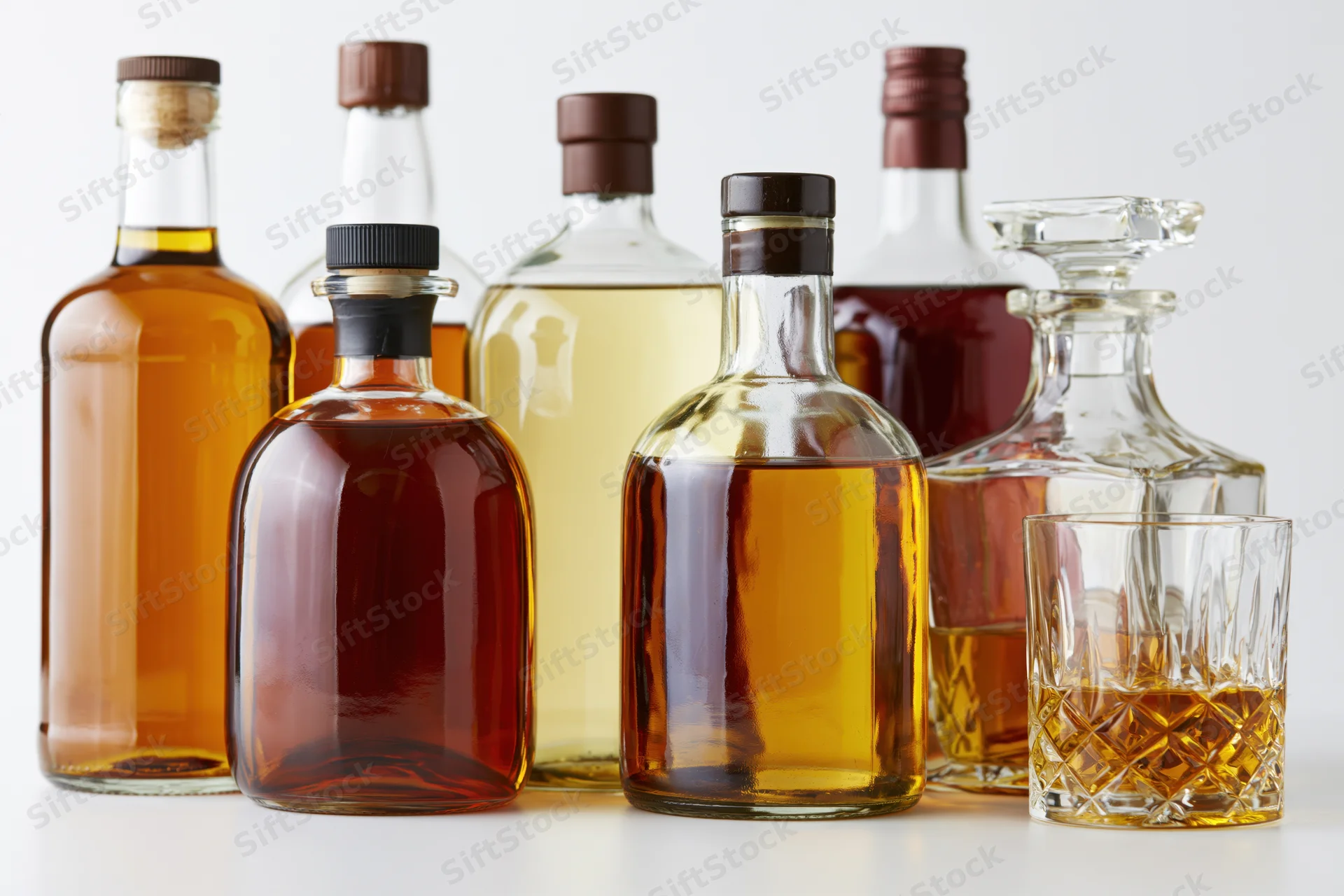 Assorted liquor bottles and a crystal decanter arranged on a white surface