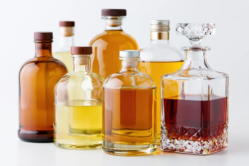 Assorted liquor bottles and a crystal decanter arranged on a white surface