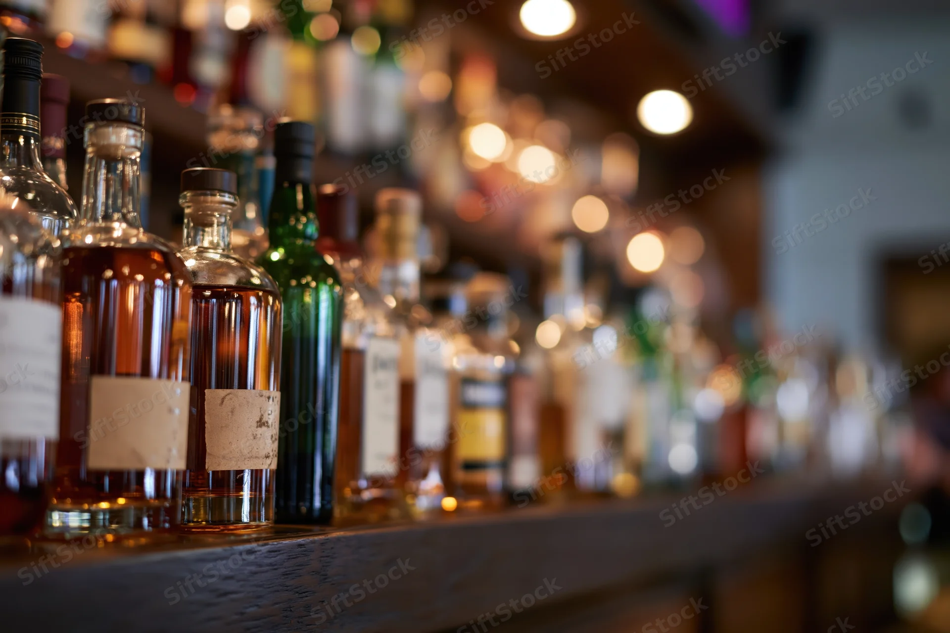 Assorted liquor bottles lined up on a wooden bar shelf in a dimly lit bar interior