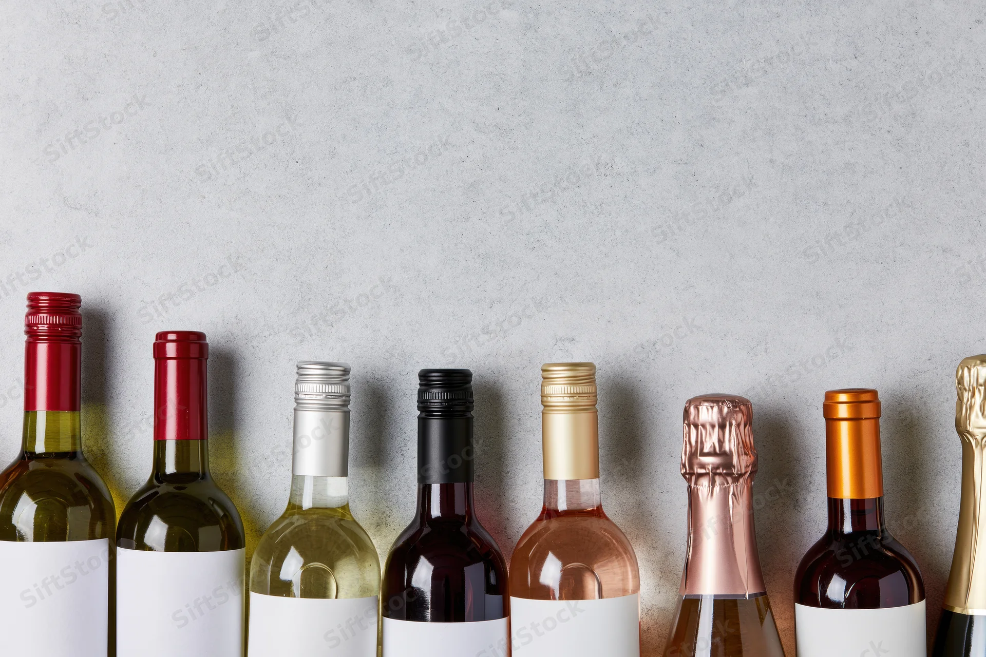 Row of wine bottles with blank labels lined up against a gray wall