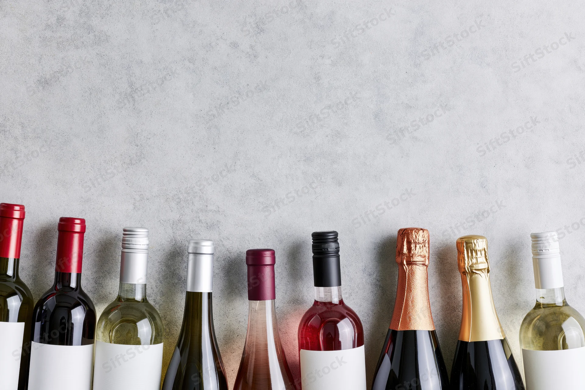 Row of wine bottles with blank labels lined up against a gray concrete background