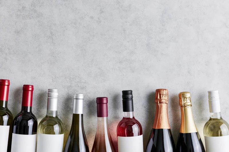 Row of wine bottles with blank labels lined up against a gray concrete background