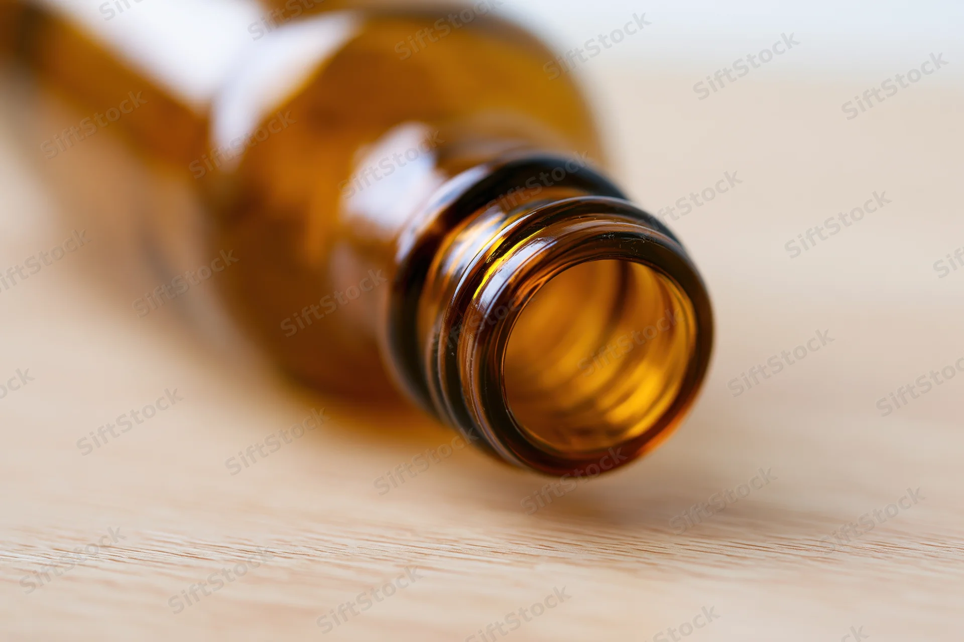 Empty amber glass bottle lying on its side on a pale wooden surface