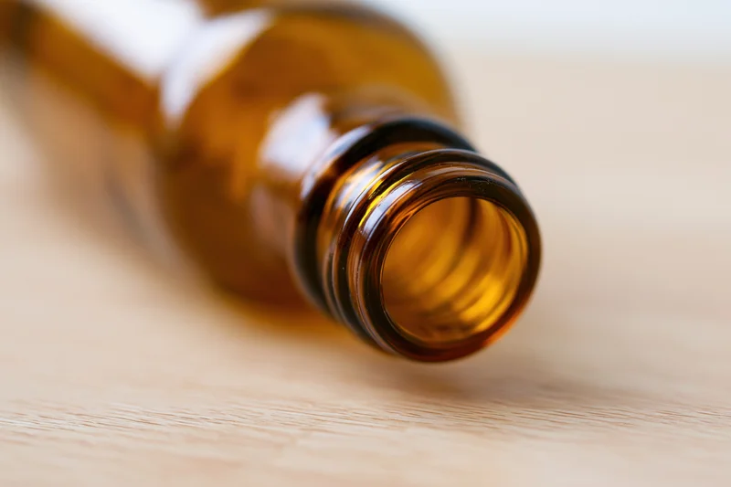 Empty amber glass bottle lying on its side on a pale wooden surface