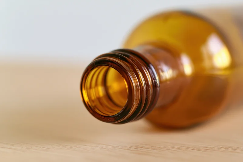 Empty amber glass bottle lying on its side on a pale wooden surface