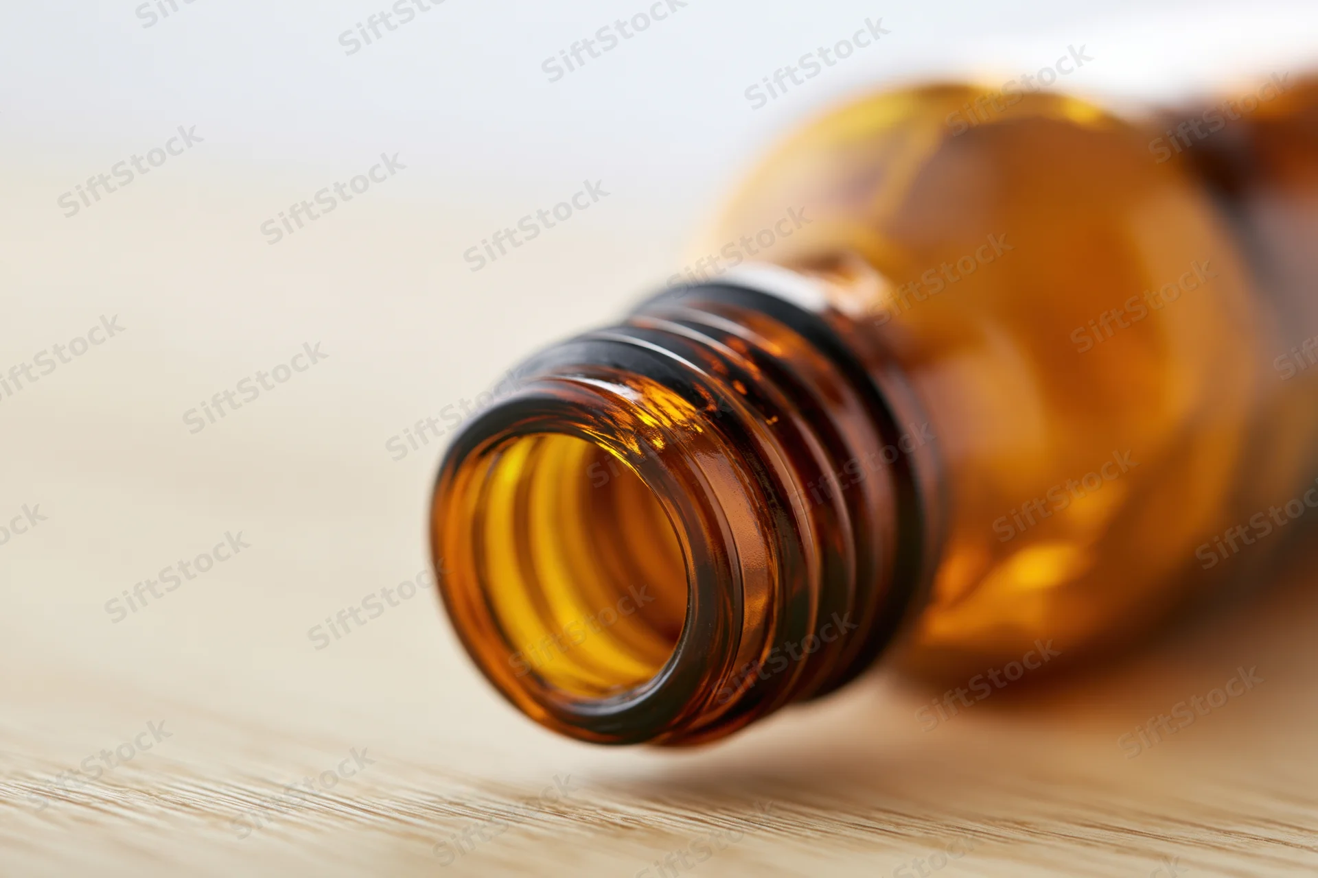 Empty amber glass bottle lying on its side on a pale wooden surface