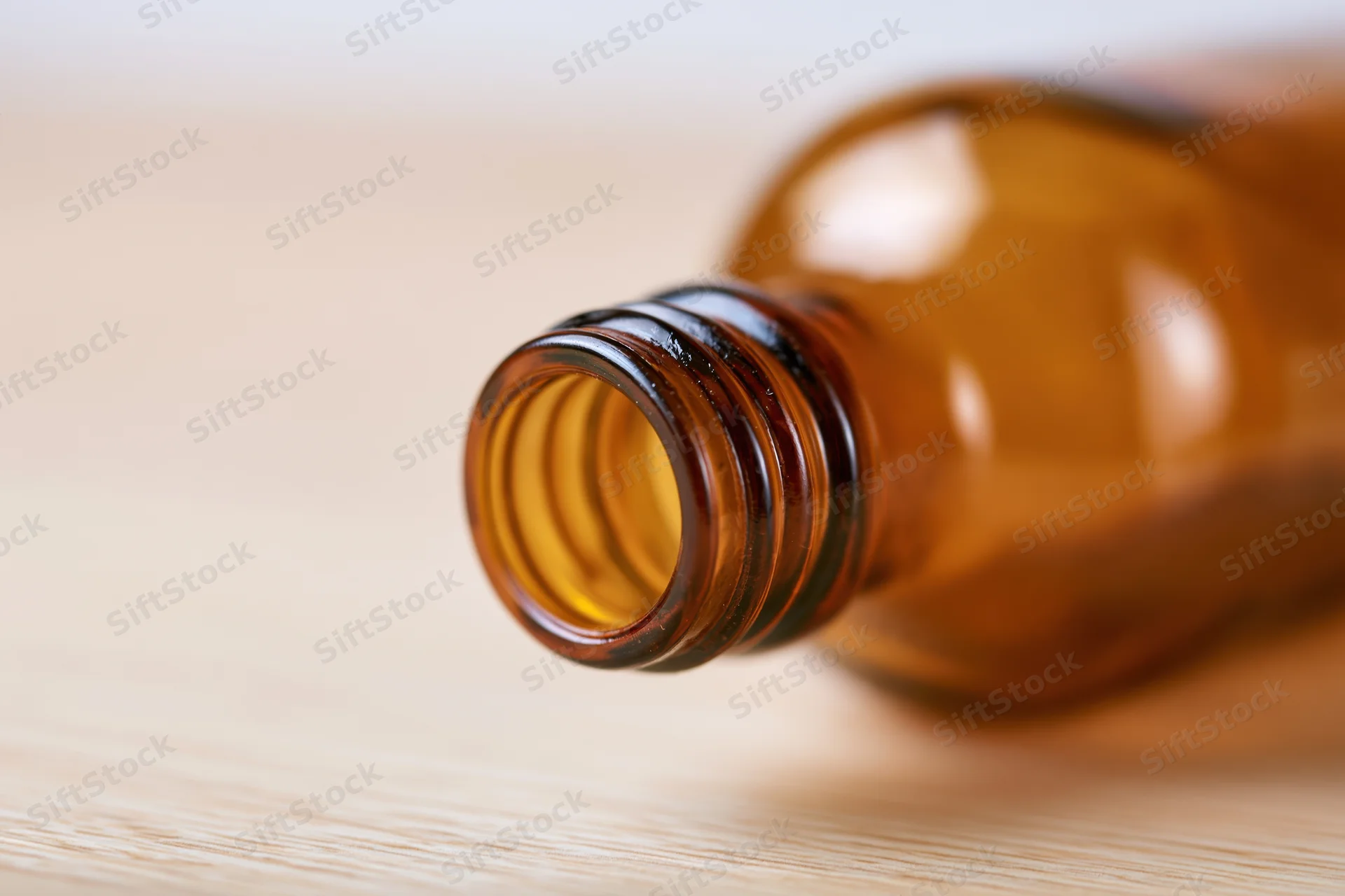 Empty amber glass bottle lying on pale wooden surface