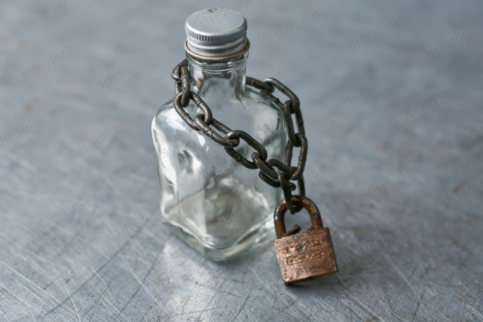 Empty glass liquor bottle secured with heavy metal chain and padlock on textured gray surface