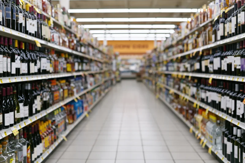 Long aisle in a liquor store lined with shelves of bottles stretching into the distance