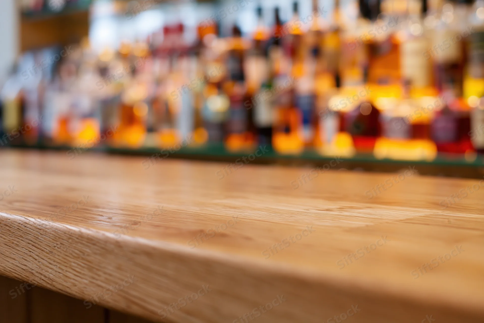 Empty wooden bar counter with blurred bottles of alcohol in background