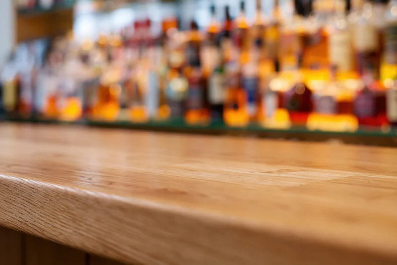 Empty wooden bar counter with blurred bottles of alcohol in background
