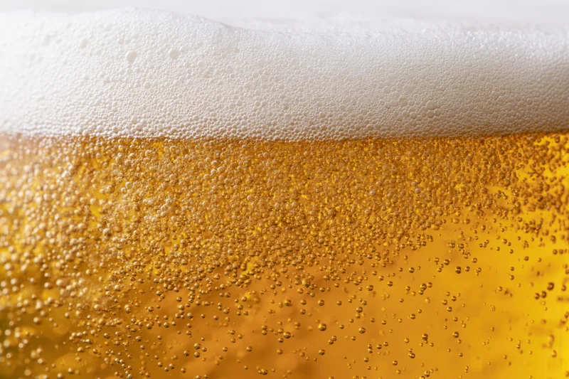 Close-up of golden lager beer with thick white foam and rising bubbles in a glass