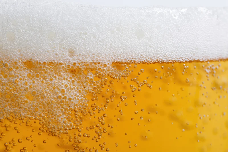 Close-up of golden lager beer with thick white foam and rising bubbles in a glass