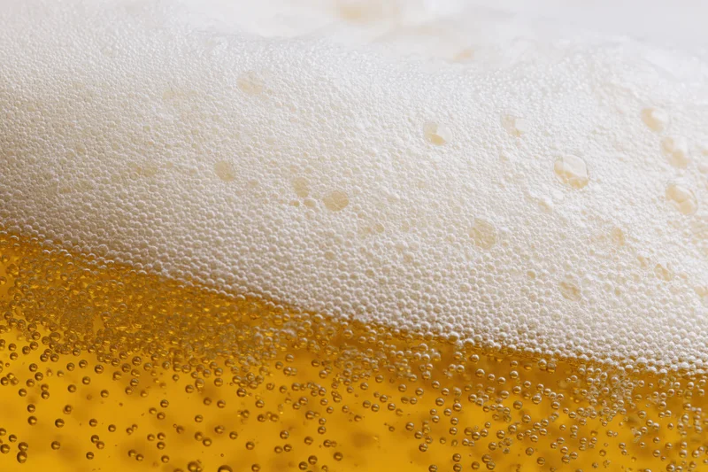Close-up of golden lager beer with thick white foam and rising bubbles in a glass