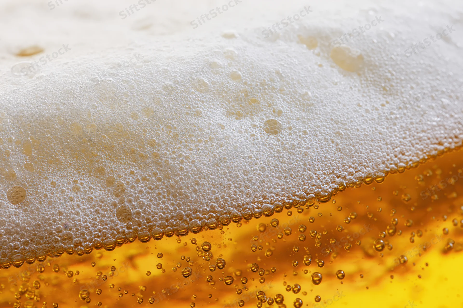 Golden lager beer with thick foam and rising bubbles in close-up view