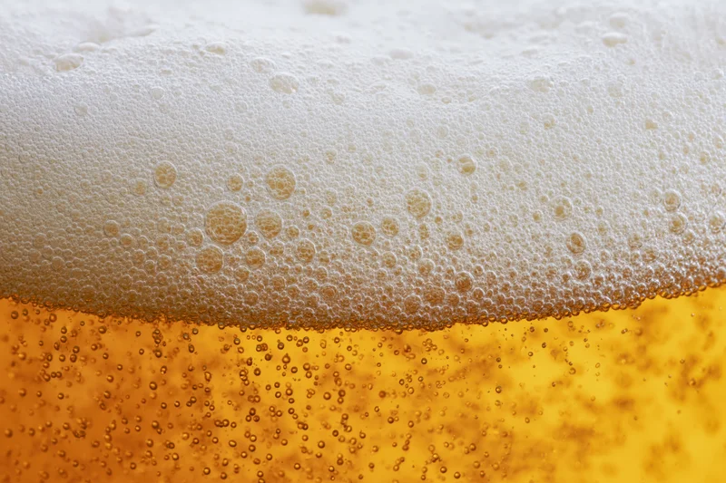 Golden lager beer with thick foam head and rising bubbles in close-up view
