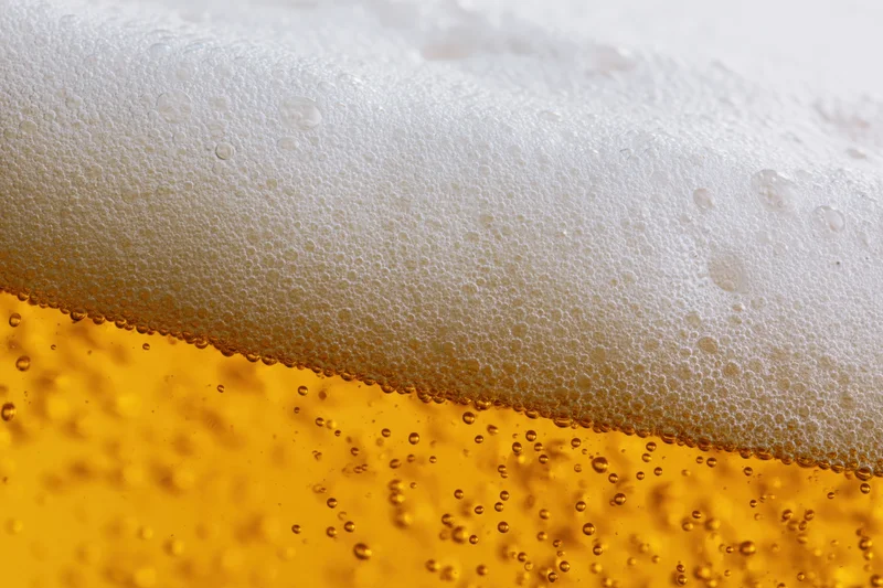 Golden lager beer with thick white foam and rising bubbles in close-up view