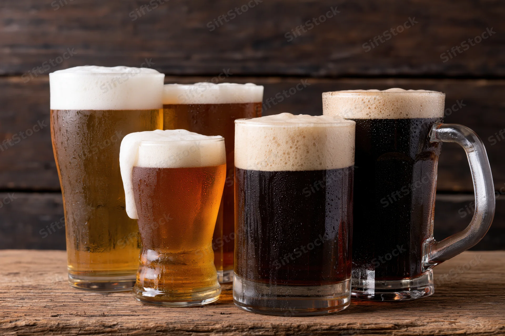 Five glasses and mugs of beer with foam arranged on a wooden table