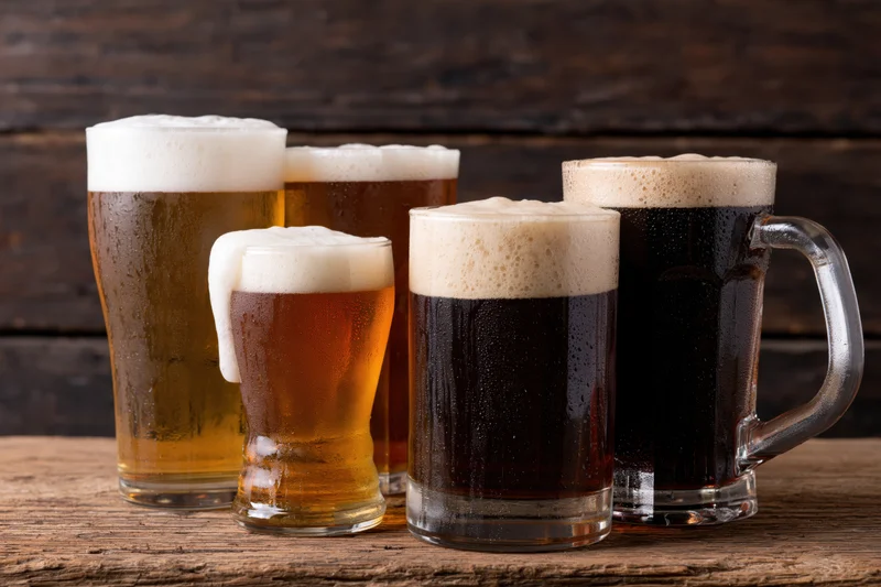 Five glasses and mugs of beer with foam arranged on a wooden table