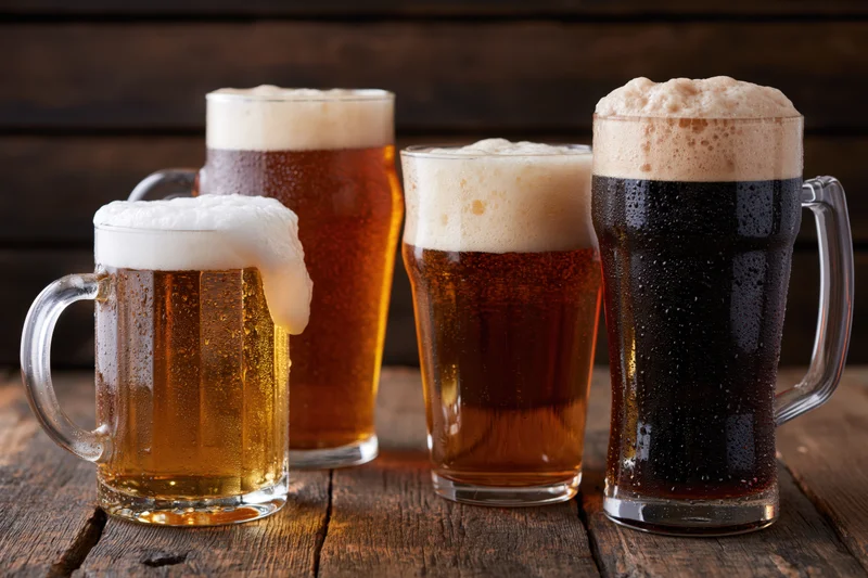 Four beer glasses and mugs with frothy heads arranged on a rustic wooden table