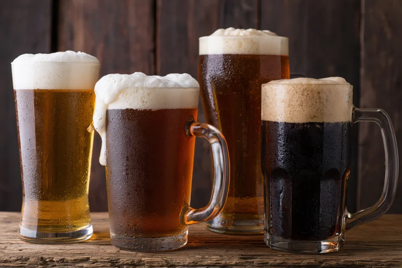 Four beer glasses and mugs with frothy heads arranged on a wooden table