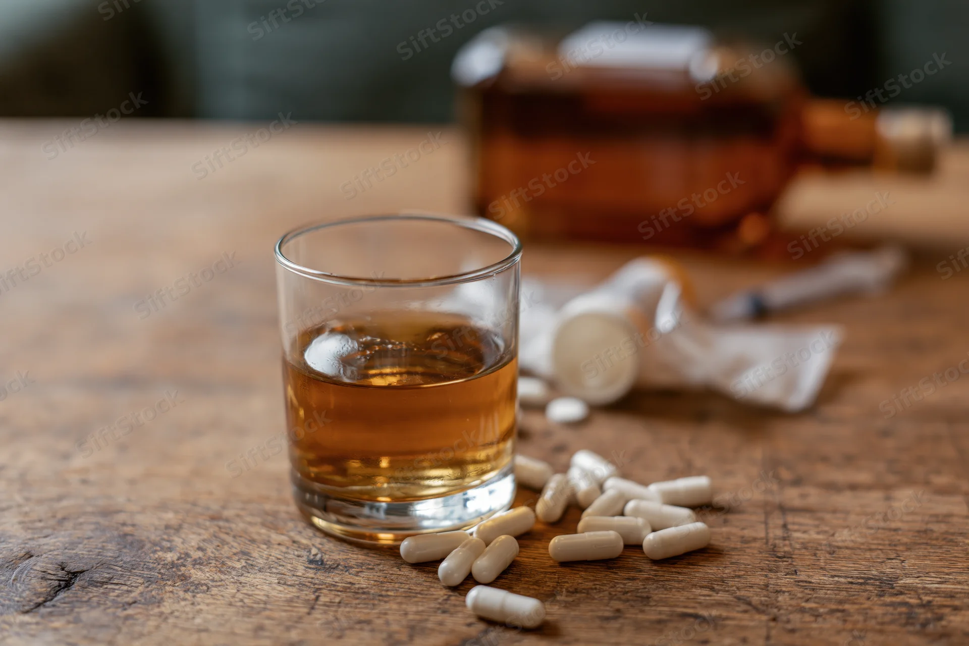 Glass of amber whiskey with scattered white capsules on a wooden table