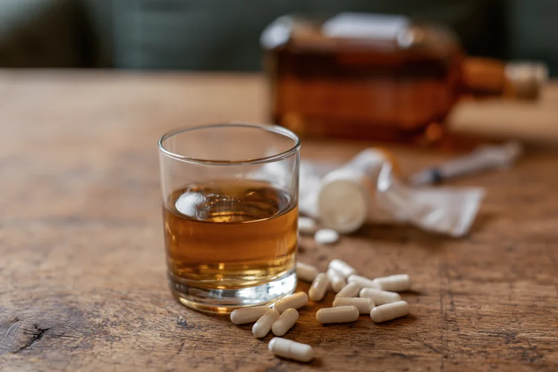 Glass of amber whiskey with scattered white capsules on a wooden table