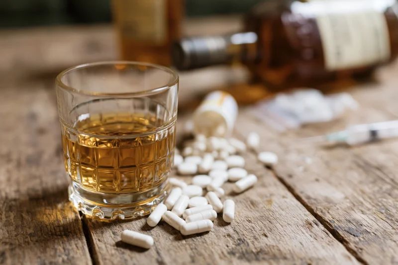 Glass of amber whiskey beside scattered white capsules on a wooden table