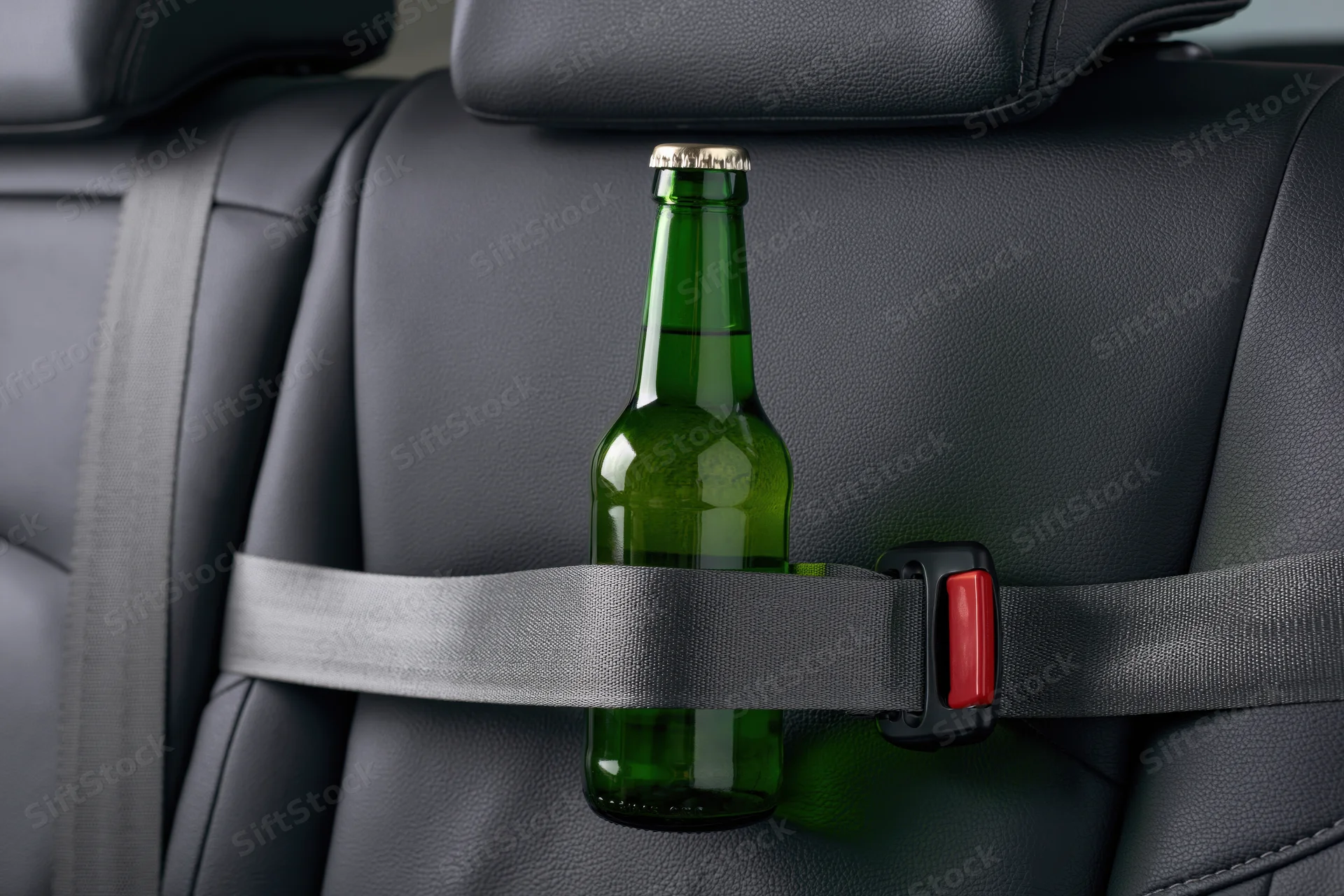Green glass beer bottle secured with gray seatbelt in car seat interior