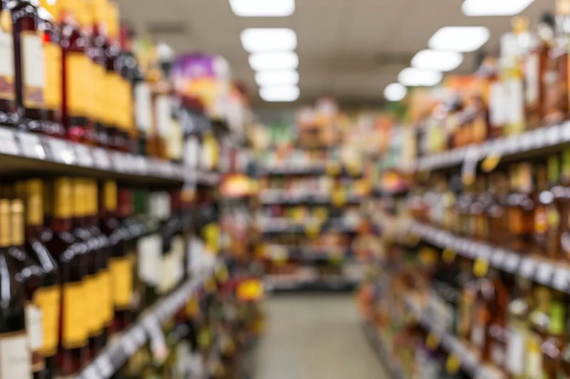 Blurred view of liquor store aisle with tall shelves lined with bottles stretching into the distance