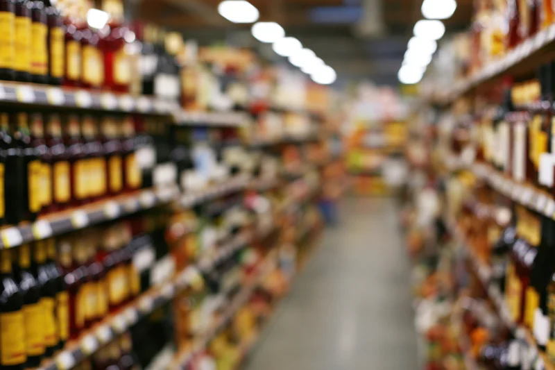 Blurred view of liquor store aisle with tall shelves lined with bottles stretching into the distance