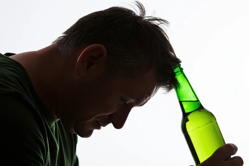 Man holding green beer bottle to his forehead in silhouette against white background
