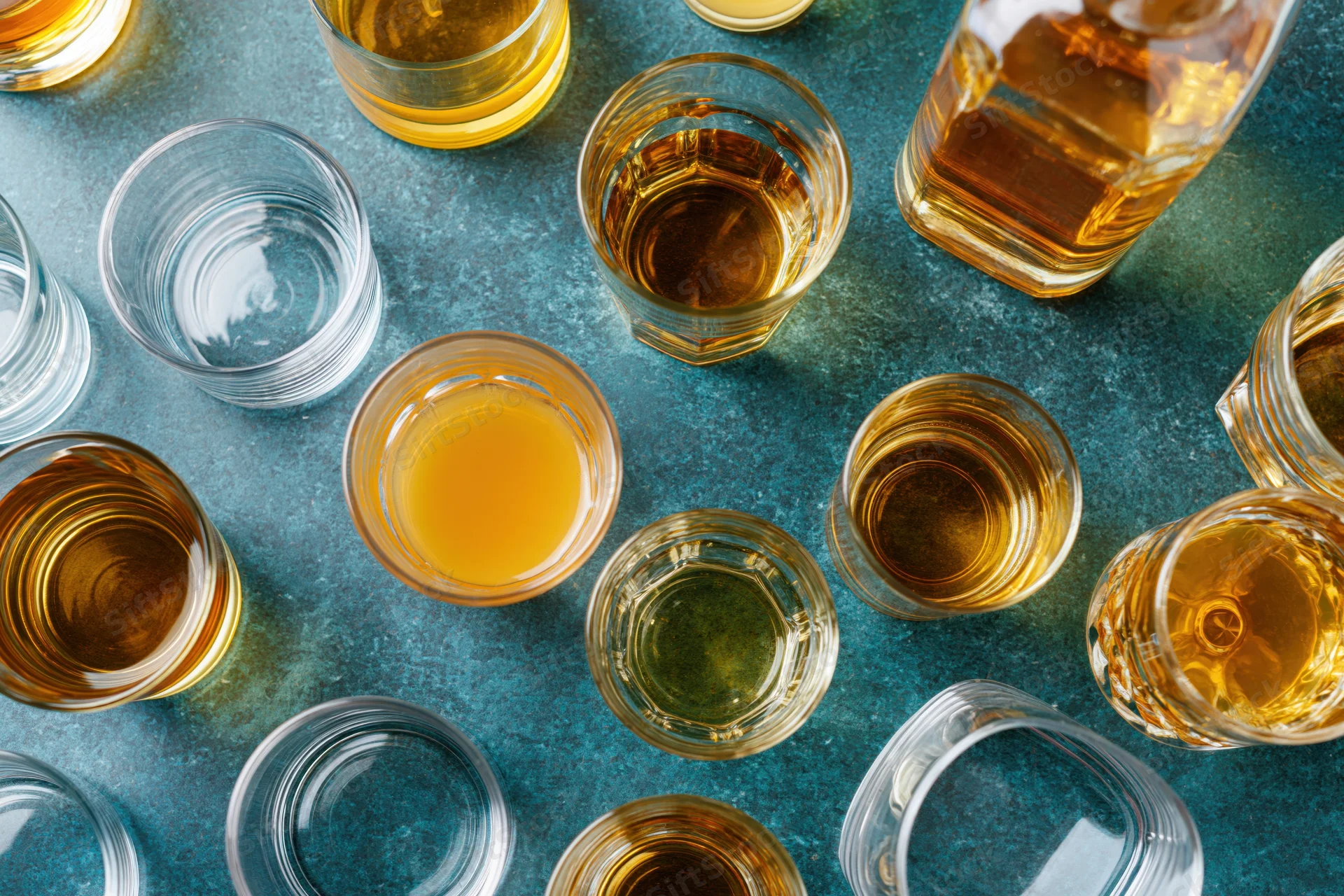 Overhead flat-lay of assorted whiskey and spirits glasses on a blue textured surface