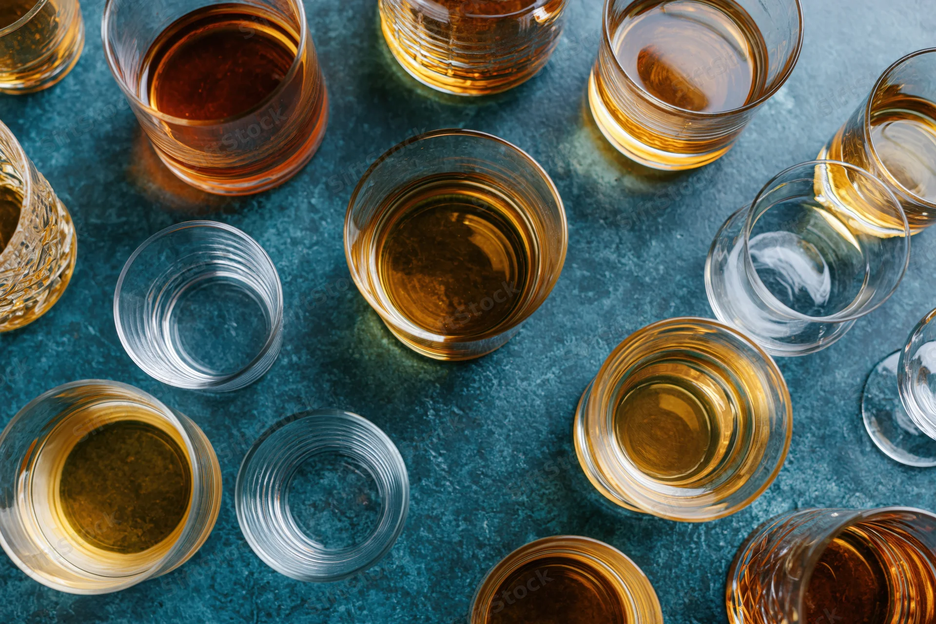 Overhead flat-lay of assorted whiskey and spirits glasses on a blue textured surface
