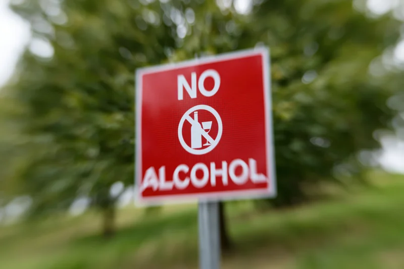 Red no alcohol prohibition sign mounted on metal post in park setting