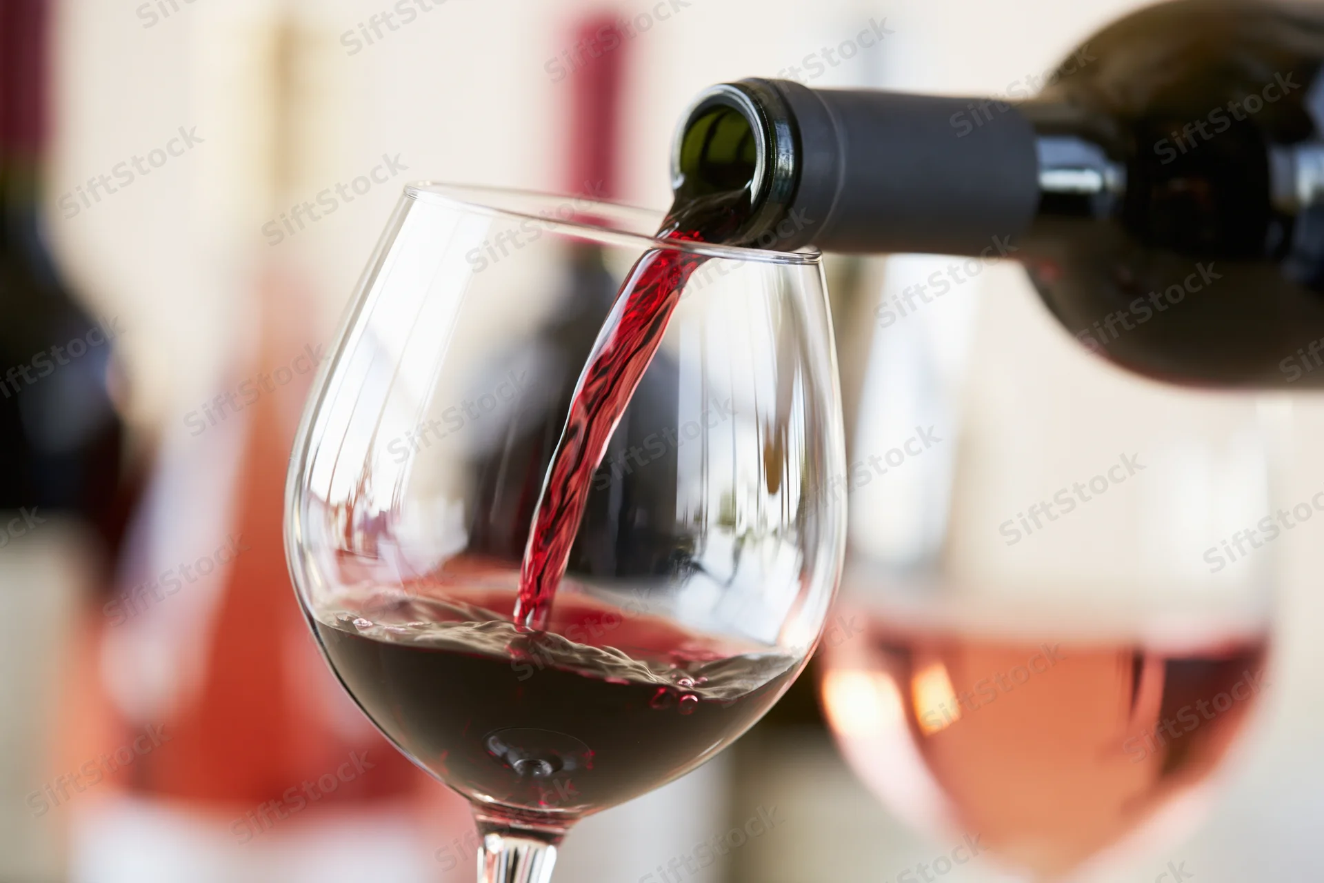 Red wine being poured from a dark green bottle into a large wine glass indoors