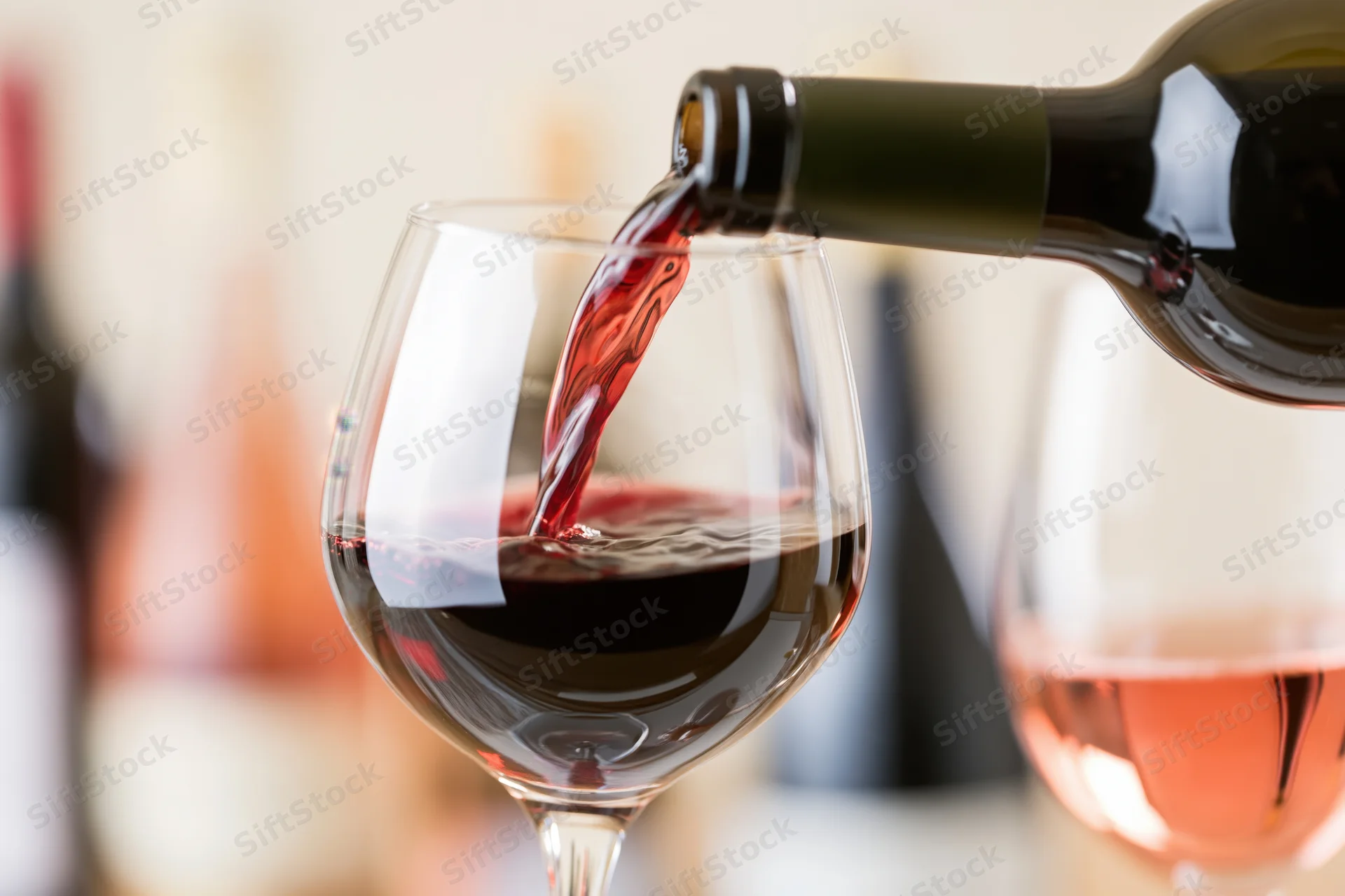 Red wine being poured from a dark green bottle into a large wine glass indoors
