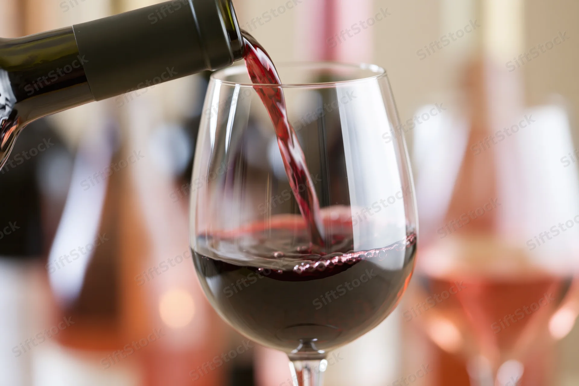 Red wine pouring from a dark green bottle into a large wine glass at a dining setting