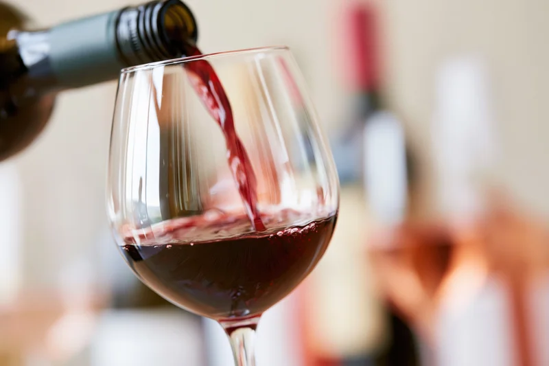 Red wine being poured from a dark green bottle into a large wine glass