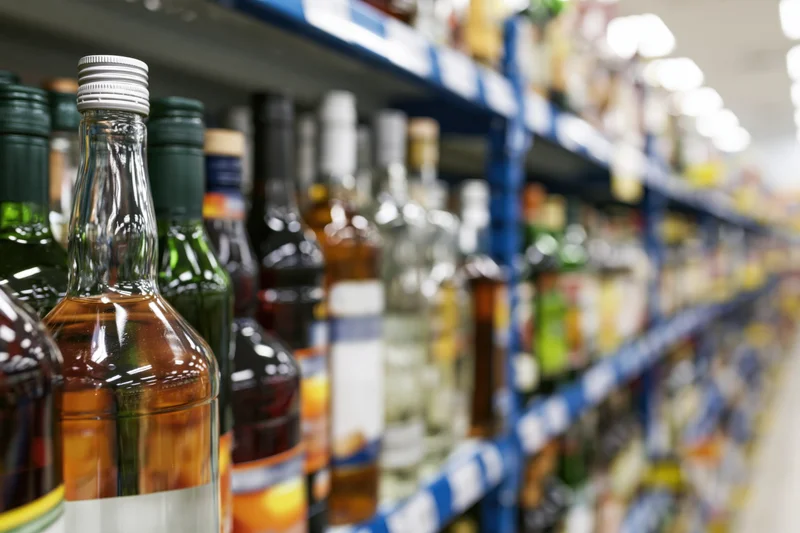 Rows of liquor bottles arranged on blue metal shelves in a store aisle