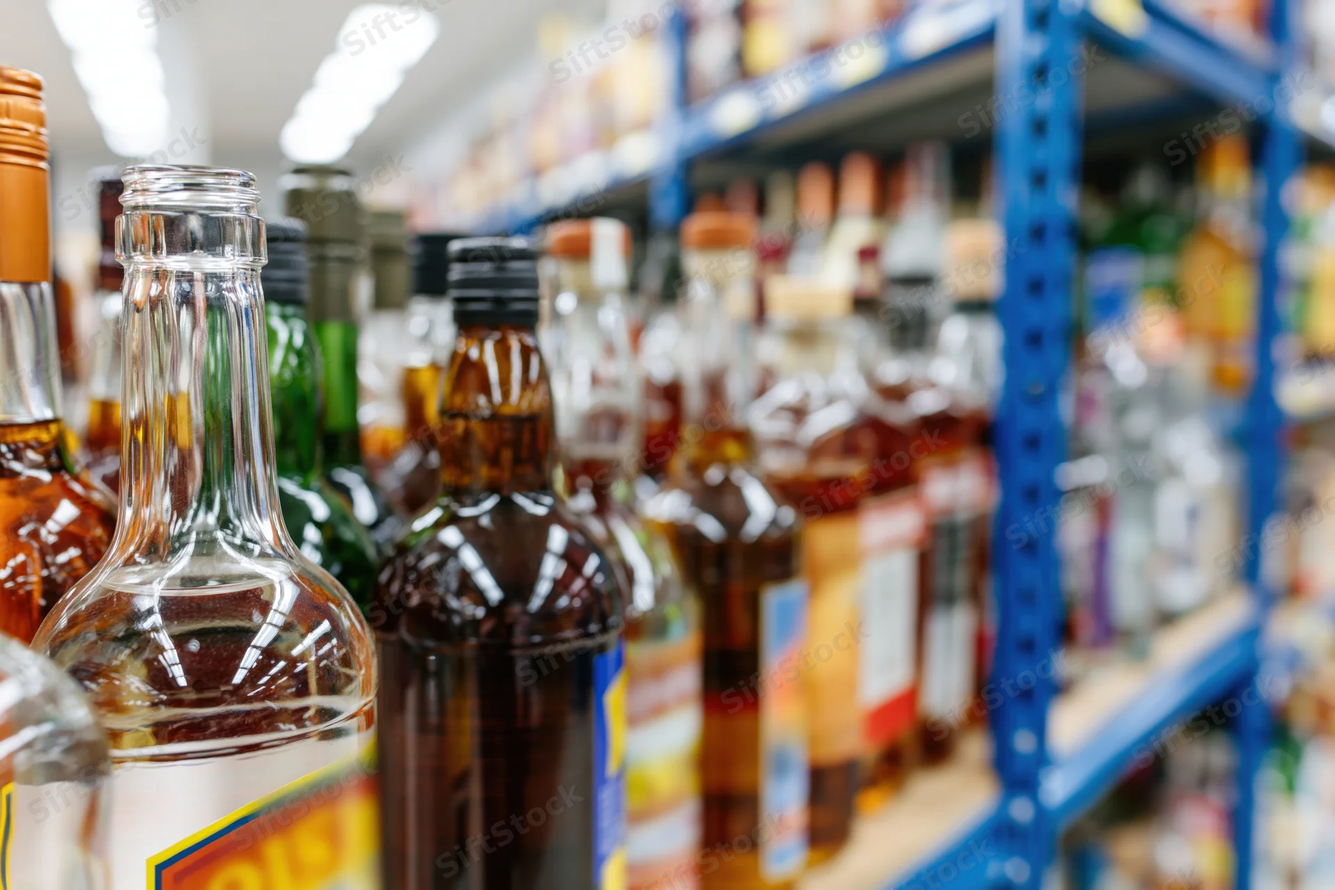 Rows of liquor bottles densely packed on blue metal shelves in a store aisle