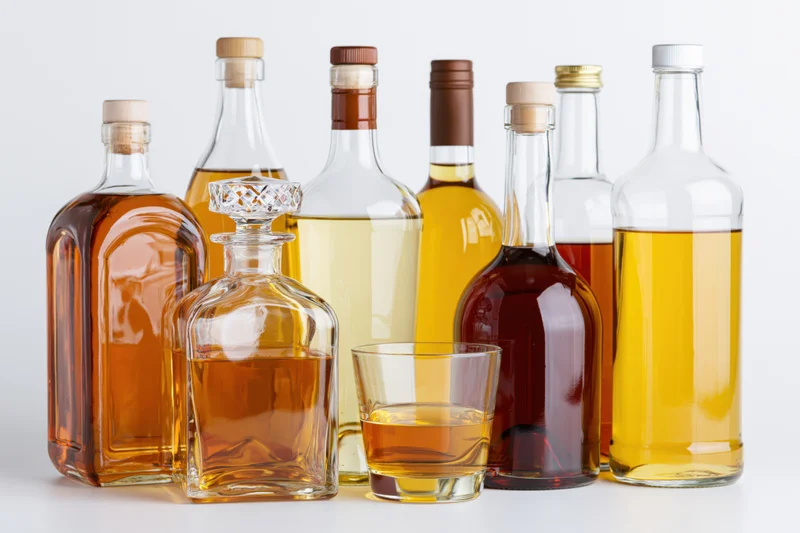 Assorted liquor bottles and a glass of amber spirit arranged on a white surface