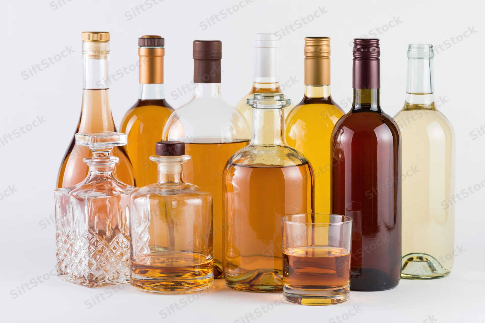 Assorted liquor bottles and a glass arranged on a white surface