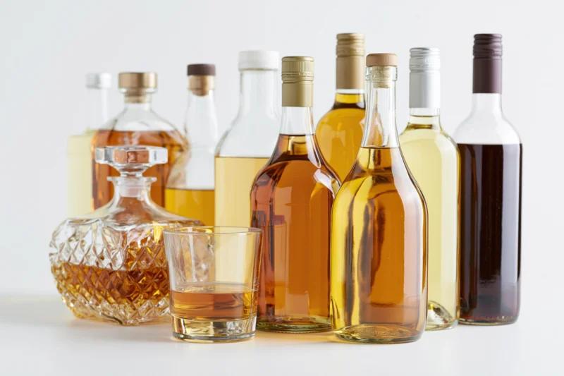 Assorted liquor bottles and a glass of whiskey arranged on a white surface