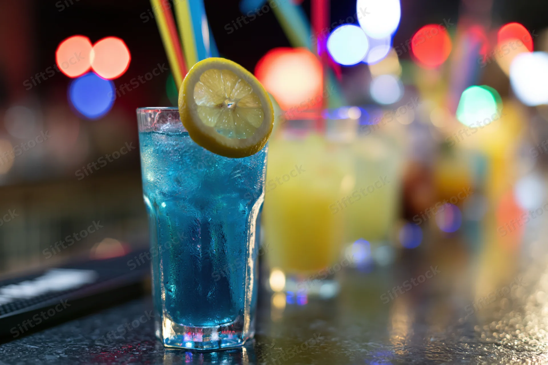 Blue cocktail with lemon garnish and straw on dark bar counter at night
