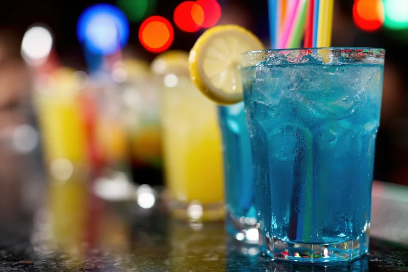 Colorful cocktails with lemon and straw on dark bar counter