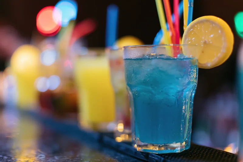 Blue cocktail with lemon and straw on dark bar counter