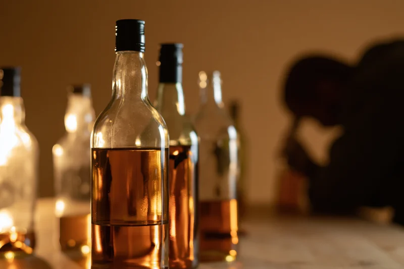 Whiskey bottles arranged on a marble table with warm lighting and a blurred silhouette in the background
