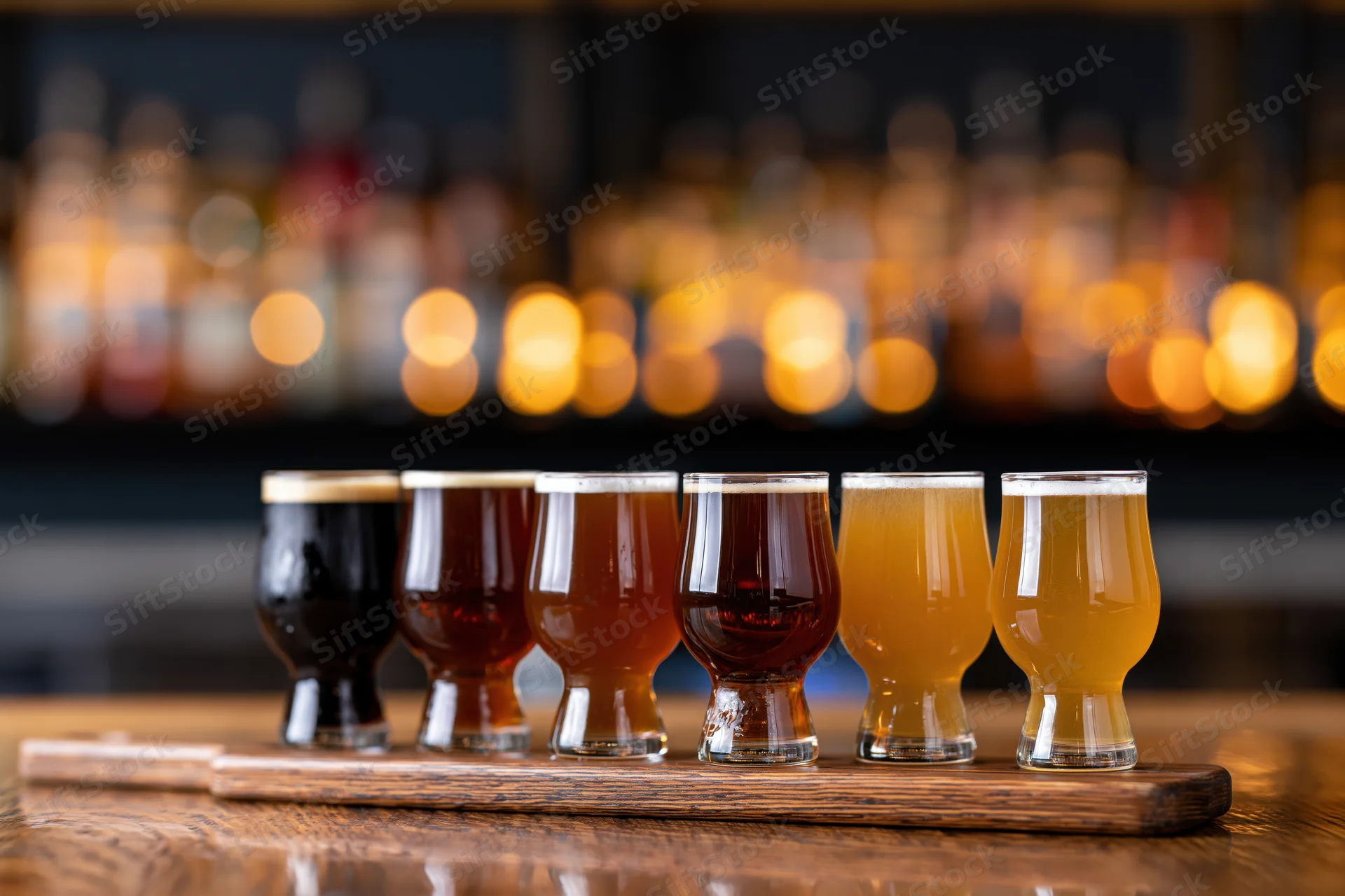 Six craft beer tasting glasses in a row on a wooden tray at a bar